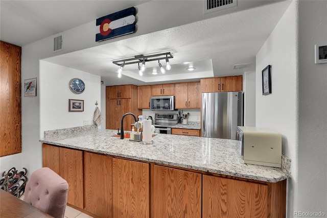 kitchen featuring light stone countertops, appliances with stainless steel finishes, a textured ceiling, and kitchen peninsula