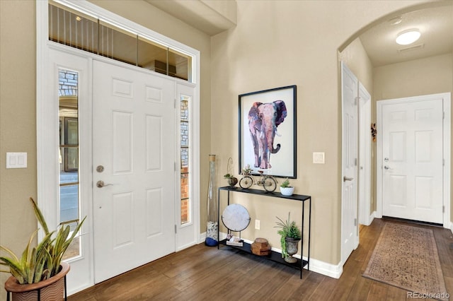 foyer entrance with dark wood finished floors, arched walkways, and baseboards