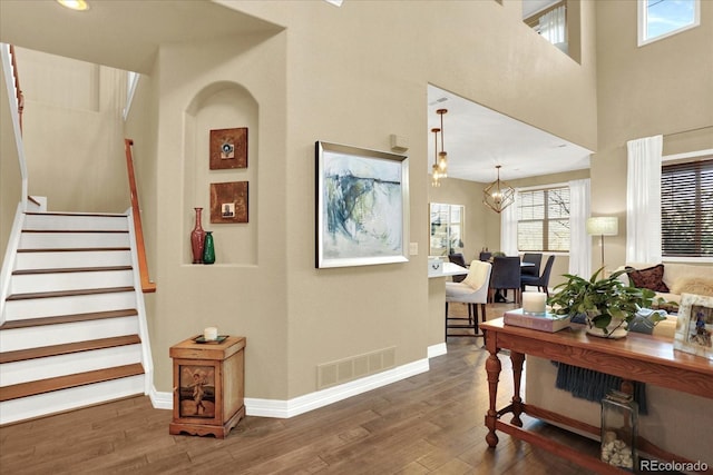 interior space with visible vents, baseboards, stairway, wood finished floors, and a notable chandelier