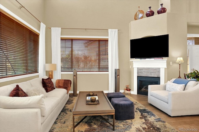 living room featuring a fireplace, wood finished floors, baseboards, and a towering ceiling