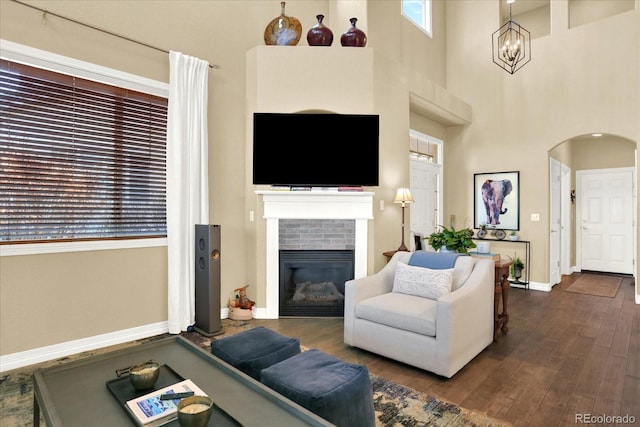 living room with dark wood-type flooring, arched walkways, an inviting chandelier, a fireplace, and baseboards