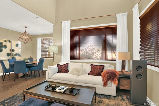 living area featuring a notable chandelier, visible vents, baseboards, and wood finished floors