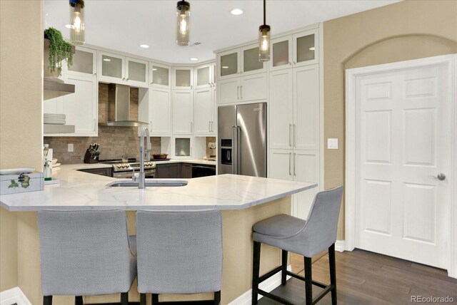 kitchen featuring light stone counters, a peninsula, appliances with stainless steel finishes, and wall chimney exhaust hood