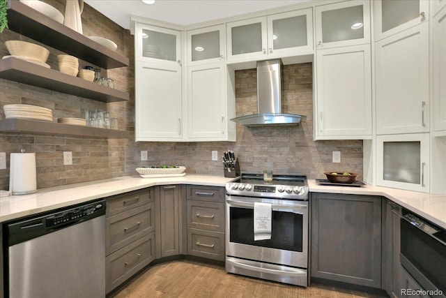 kitchen featuring gray cabinetry, decorative backsplash, stainless steel appliances, wall chimney exhaust hood, and open shelves