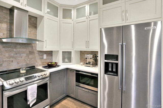 kitchen with light wood-style flooring, light countertops, appliances with stainless steel finishes, wall chimney exhaust hood, and tasteful backsplash