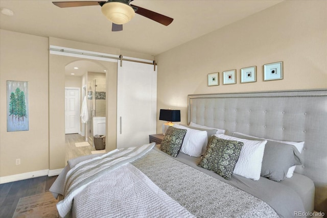 bedroom with ceiling fan, a barn door, ensuite bathroom, wood finished floors, and arched walkways