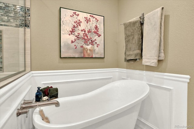 bathroom featuring a wainscoted wall, a freestanding bath, and a decorative wall