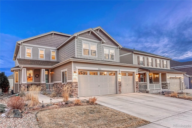 craftsman house featuring covered porch, driveway, and stone siding