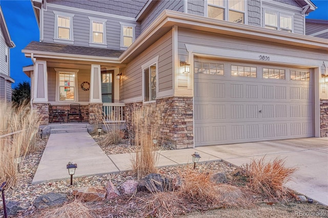 doorway to property featuring concrete driveway, stone siding, a porch, and an attached garage