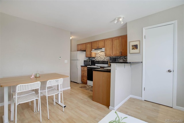 kitchen with under cabinet range hood, freestanding refrigerator, electric range oven, stainless steel microwave, and dark countertops