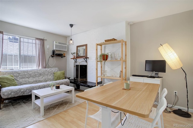 living room featuring light wood-type flooring, a brick fireplace, baseboards, and a wall mounted AC