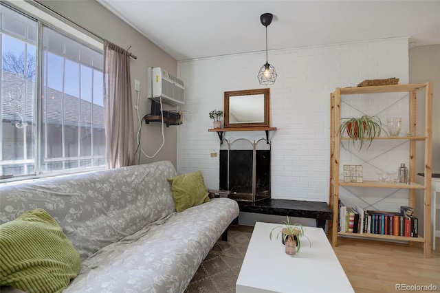 living room featuring a fireplace with raised hearth, brick wall, a wall unit AC, and wood finished floors