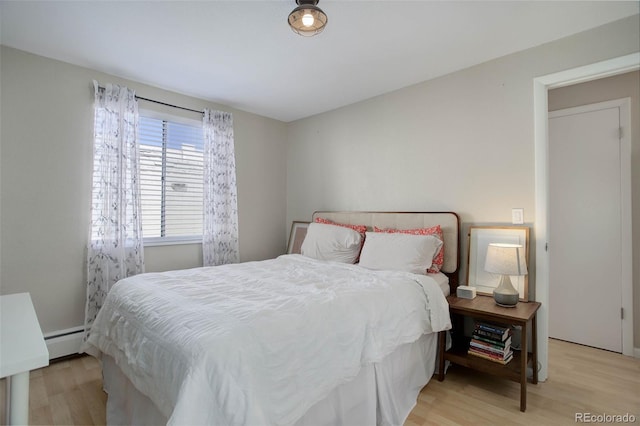 bedroom with a baseboard heating unit and light wood finished floors