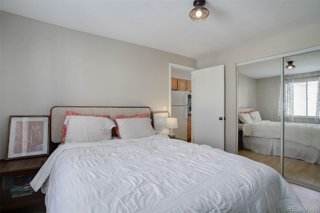 bedroom with a closet, wood finished floors, and freestanding refrigerator