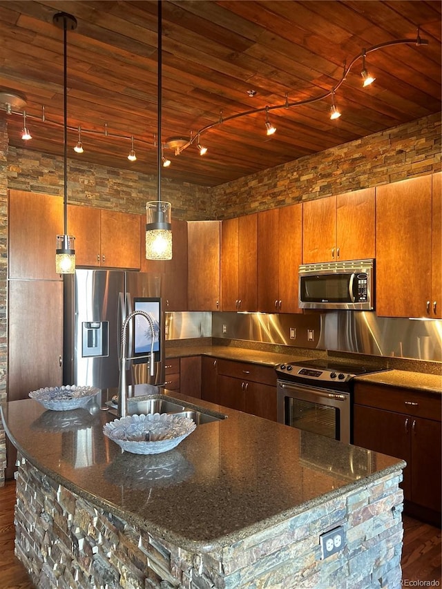 kitchen with an island with sink, appliances with stainless steel finishes, sink, and pendant lighting