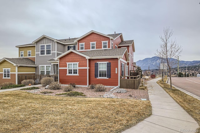 view of front facade featuring a shingled roof, a mountain view, and a front lawn