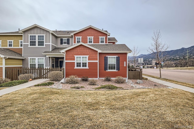 view of front of home with a front lawn, roof with shingles, fence, and a mountain view