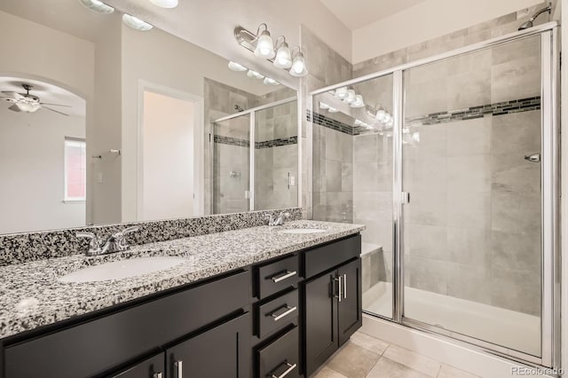 full bath with double vanity, a stall shower, ceiling fan, and a sink