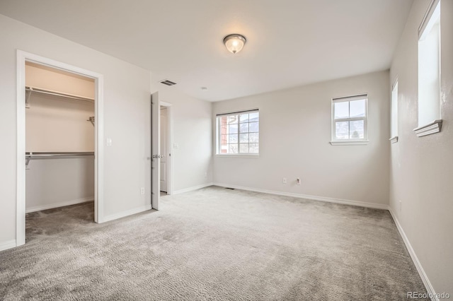 unfurnished bedroom featuring visible vents, multiple windows, a spacious closet, and carpet flooring