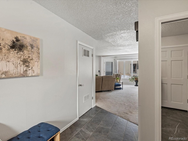 hall with visible vents, dark carpet, a textured ceiling, and baseboards