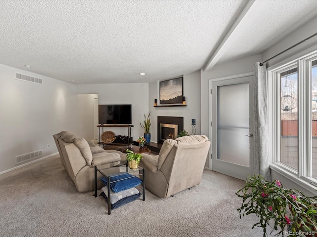 living area featuring a warm lit fireplace, visible vents, and light colored carpet