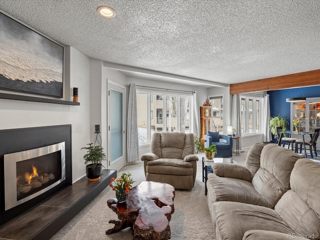 living room with a lit fireplace, a textured ceiling, baseboards, and carpet flooring