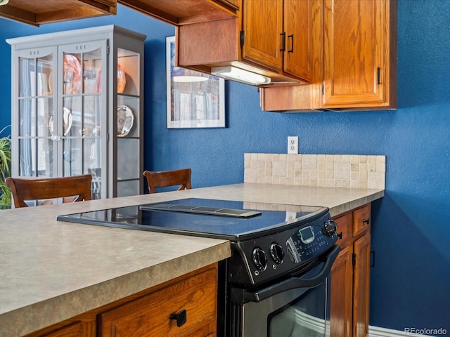 kitchen featuring a textured wall, black / electric stove, light countertops, decorative backsplash, and brown cabinetry