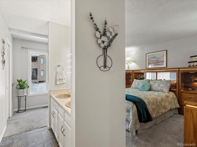 bedroom with a textured ceiling, stone finish floor, a sink, and baseboards