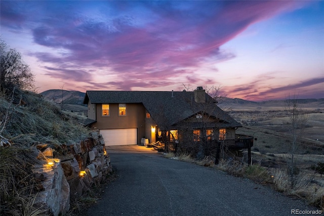 chalet / cabin with aphalt driveway, a mountain view, a garage, stucco siding, and a chimney