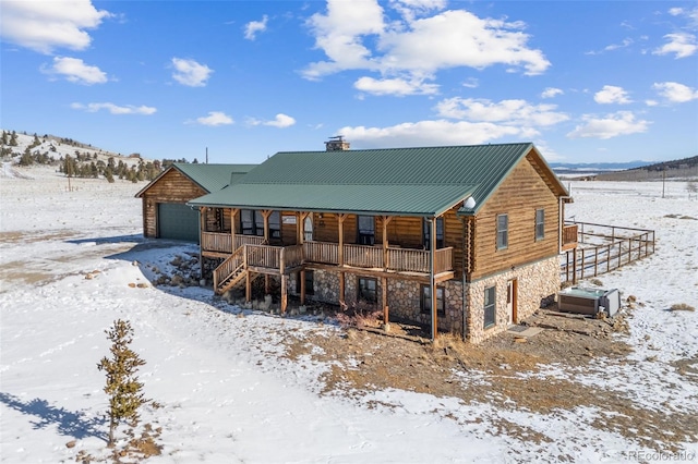 snow covered property with covered porch, a garage, and a mountain view