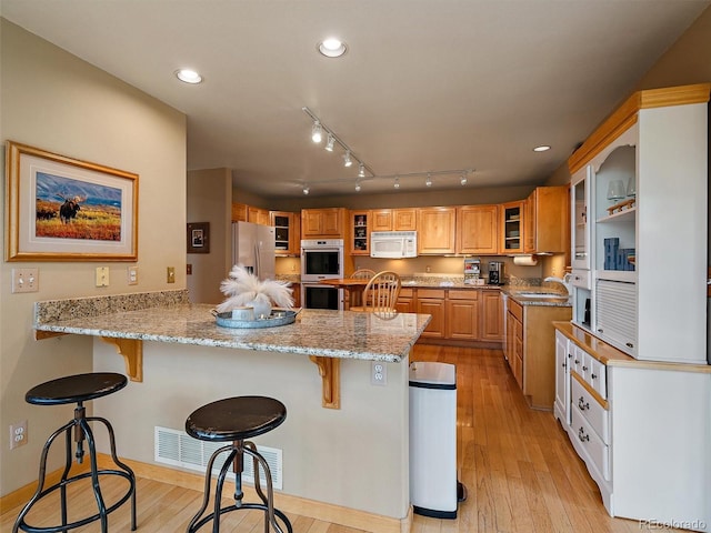 13094 Molly Dr, Conifer, CO 80433 - kitchen with appliances with stainless steel finishes, a peninsula, a kitchen breakfast bar, light stone counters, and light wood finished floors