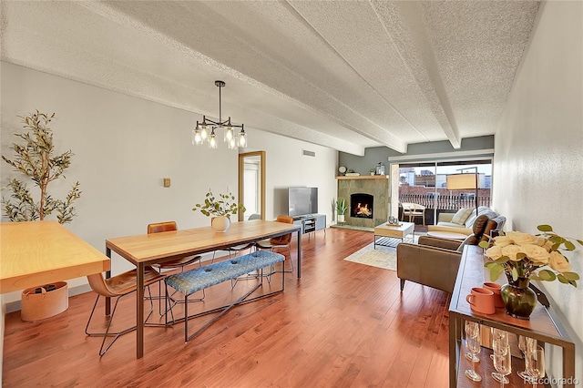 dining space with a tile fireplace, an inviting chandelier, lofted ceiling with beams, a textured ceiling, and wood-type flooring