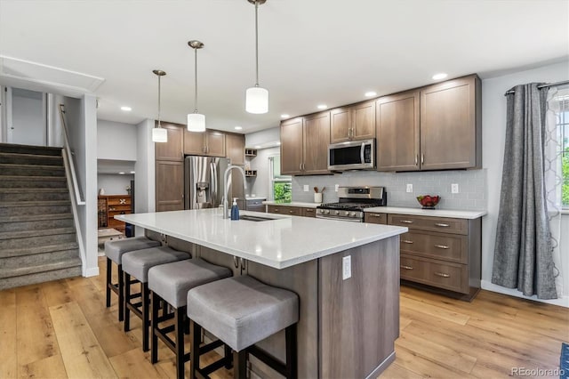 kitchen with appliances with stainless steel finishes, a sink, light wood-style flooring, tasteful backsplash, and recessed lighting