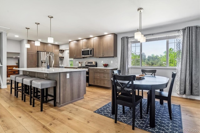kitchen featuring appliances with stainless steel finishes, light countertops, light wood-style floors, tasteful backsplash, and a kitchen island with sink