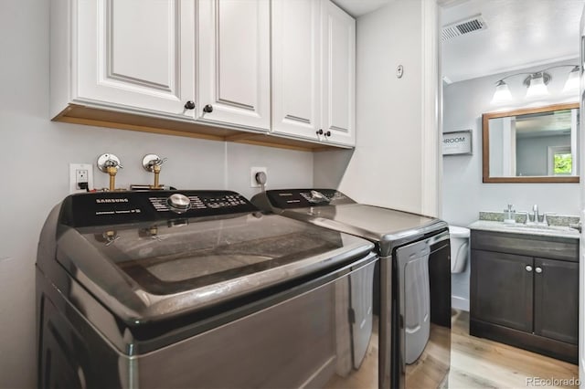 clothes washing area featuring washer and clothes dryer, light wood-style flooring, and cabinet space