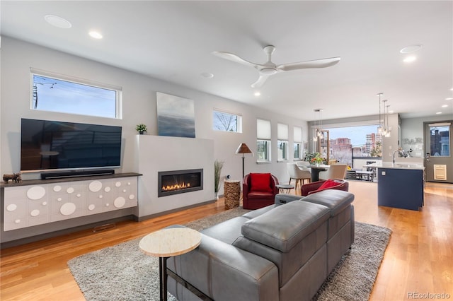 living area featuring light wood finished floors, recessed lighting, a ceiling fan, and a glass covered fireplace