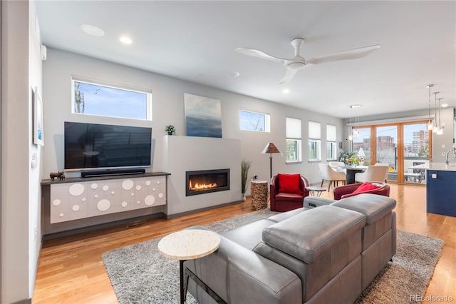 living area with light wood finished floors, recessed lighting, ceiling fan with notable chandelier, and a glass covered fireplace