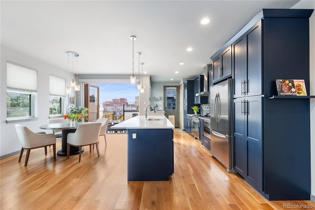 kitchen with stainless steel appliances, light countertops, light wood-style flooring, a kitchen island with sink, and a sink