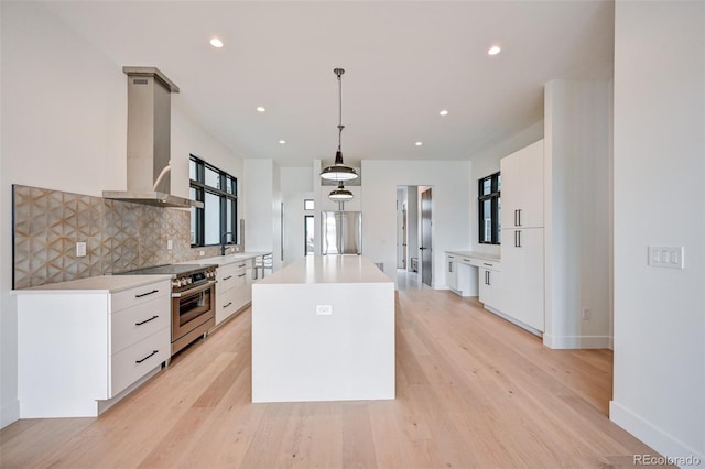 kitchen with hanging light fixtures, white cabinets, wall chimney exhaust hood, high end range, and a center island