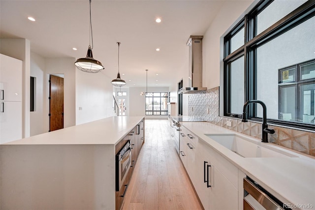 kitchen with pendant lighting, sink, a large island, white cabinetry, and light wood-type flooring