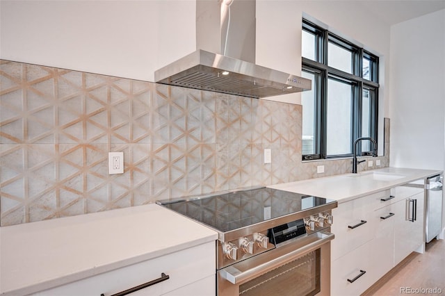 kitchen with sink, wall chimney exhaust hood, white cabinets, stainless steel stove, and decorative backsplash