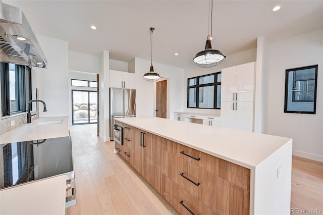 kitchen with white cabinets, wall chimney range hood, pendant lighting, and light wood-type flooring