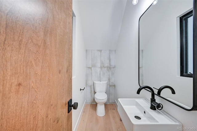 bathroom with lofted ceiling, toilet, tile walls, hardwood / wood-style flooring, and sink