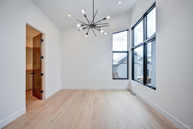 empty room with light wood-type flooring, a chandelier, and lofted ceiling