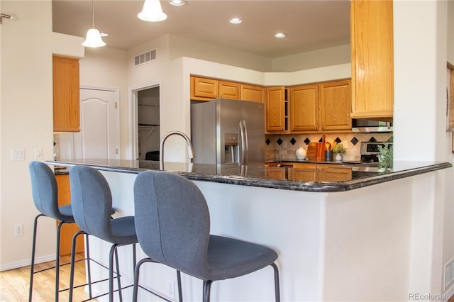 698 Larimer Creek Dr, Monument, CO 80132 - kitchen with appliances with stainless steel finishes, backsplash, a kitchen breakfast bar, dark stone counters, and light wood-style floors