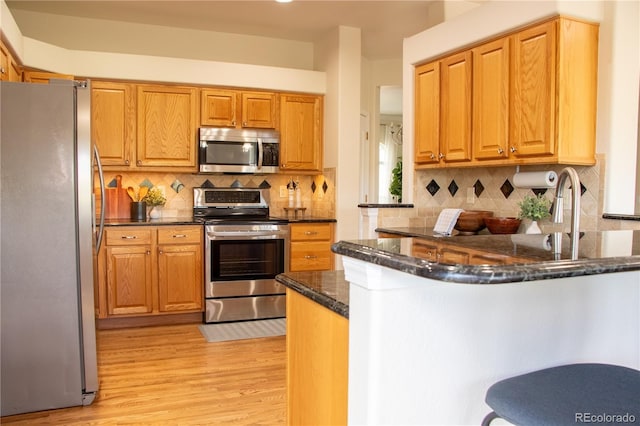 698 Larimer Creek Dr, Monument, CO 80132 - kitchen featuring appliances with stainless steel finishes, a peninsula, light wood finished floors, tasteful backsplash, and dark stone countertops