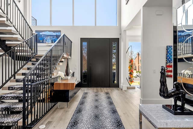 entrance foyer with stairs, a towering ceiling, baseboards, and wood finished floors