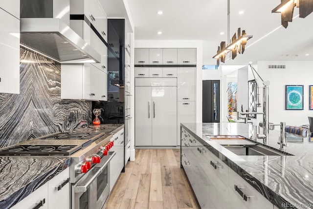 kitchen featuring dark stone counters, high end appliances, light wood-type flooring, wall chimney range hood, and visible vents