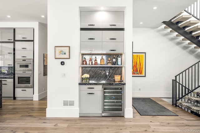 bar featuring bar area, stairway, stainless steel double oven, visible vents, and wine cooler