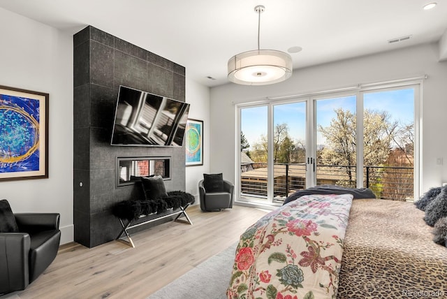 bedroom with a fireplace, light wood-style flooring, and access to exterior